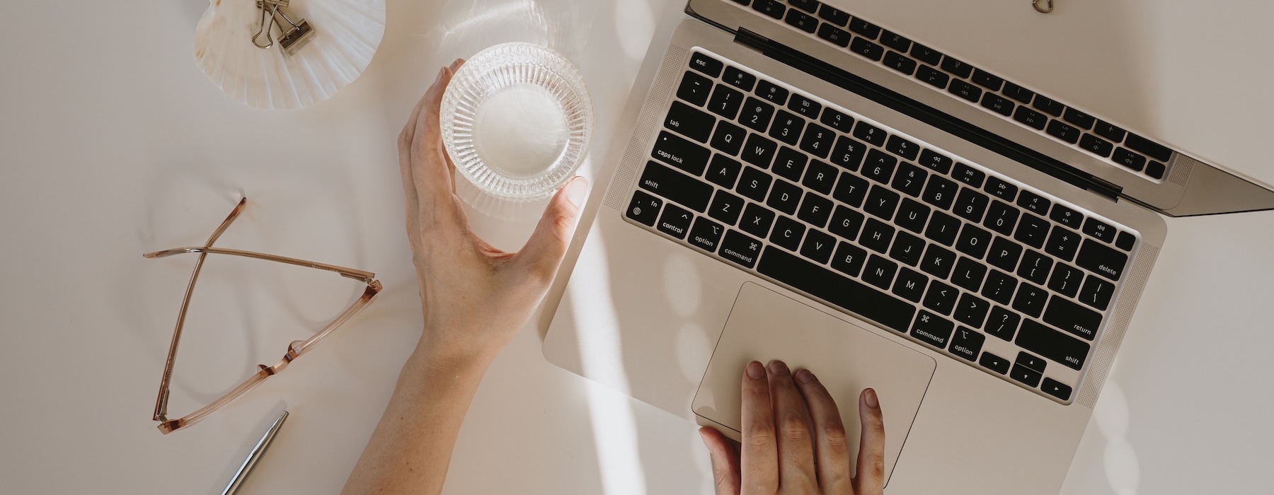 a person typing on a laptop and reaching for a drink
